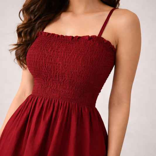 Maroon smocked midi dress with thin straps on a neutral background